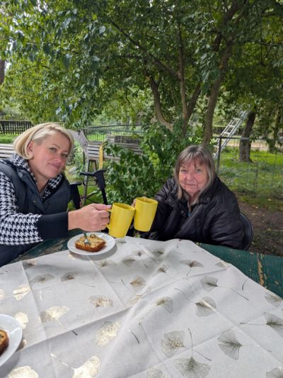 Bewohnerin und Mitarbeiterin sitzen am Tisch, trinken Kaffee und  essen Kuchen